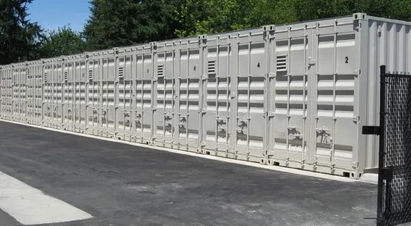 Row of steel shipping container storage units with gated access at Willow Creek Self Storage